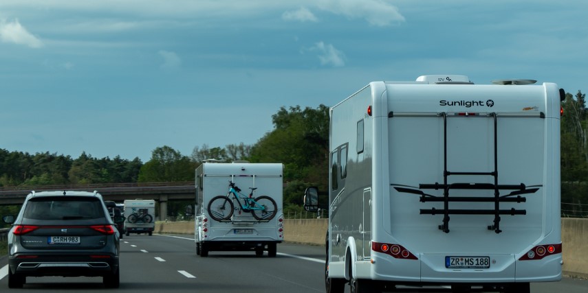 Two white RVs travel down the highway, sharing the road with cars.
