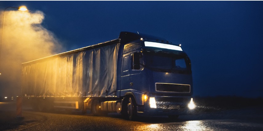 A dark blue semi truck on a road in twilight with an emissions cloud billowing nearby.