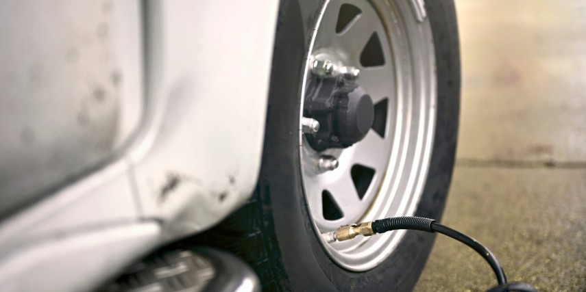 An RV is parked on pavement while the tire is hooked up to an air compressor.